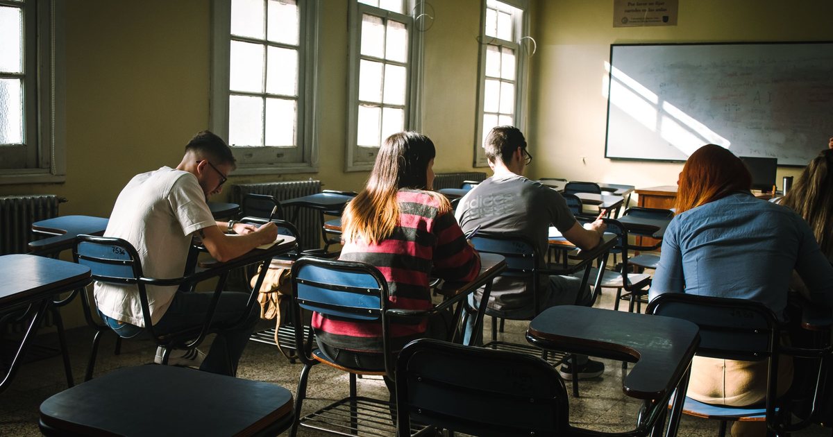 Studenti píšící zkoušku v jednotlivých lavicích ve sluncem prozářené učebně